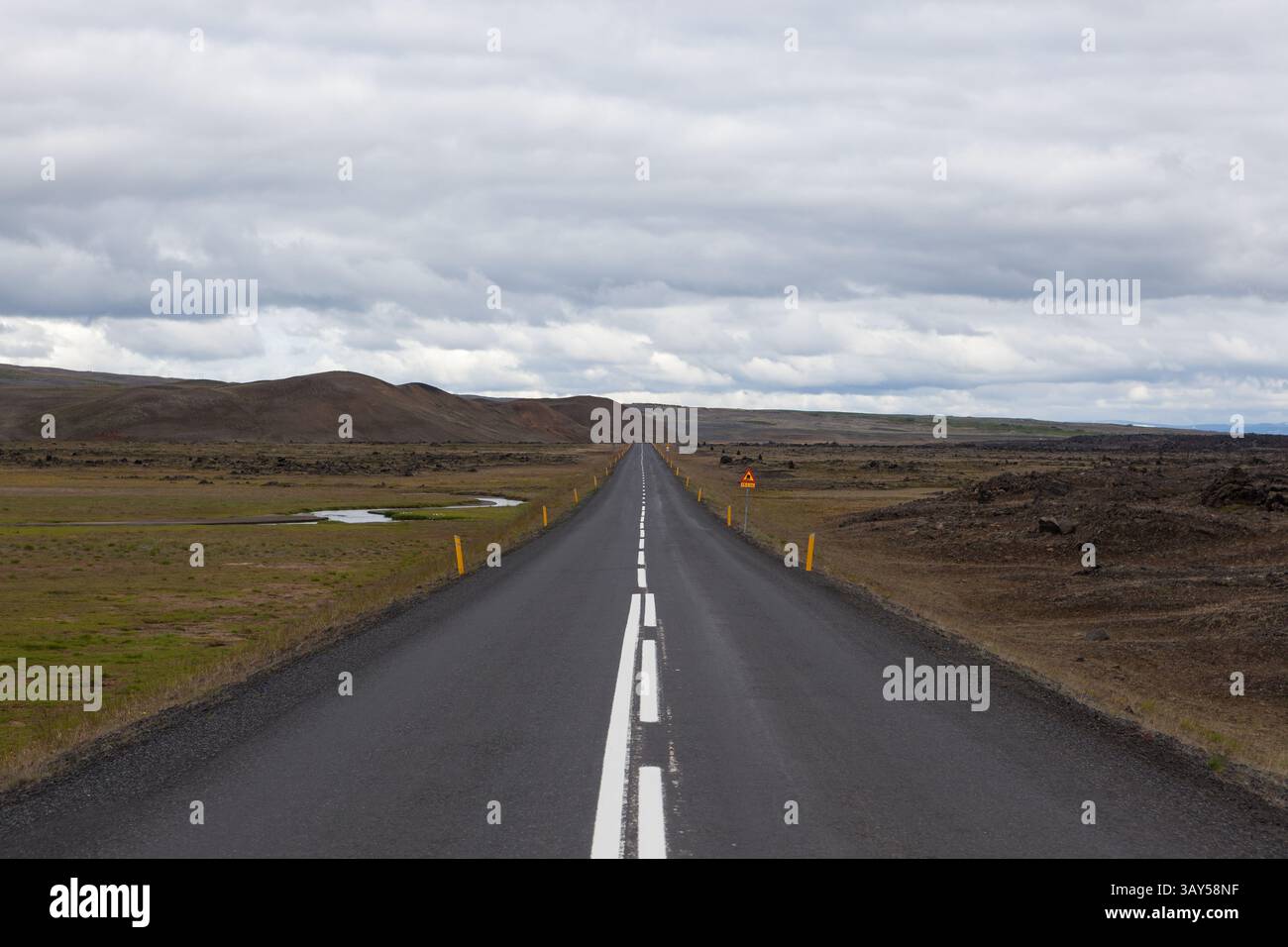 Islanda strada con montagne all'orizzonte. Strada rettilinea vuota nel paesaggio rurale islandese con cartelli. Nuvoloso giorno d'estate. Foto Stock