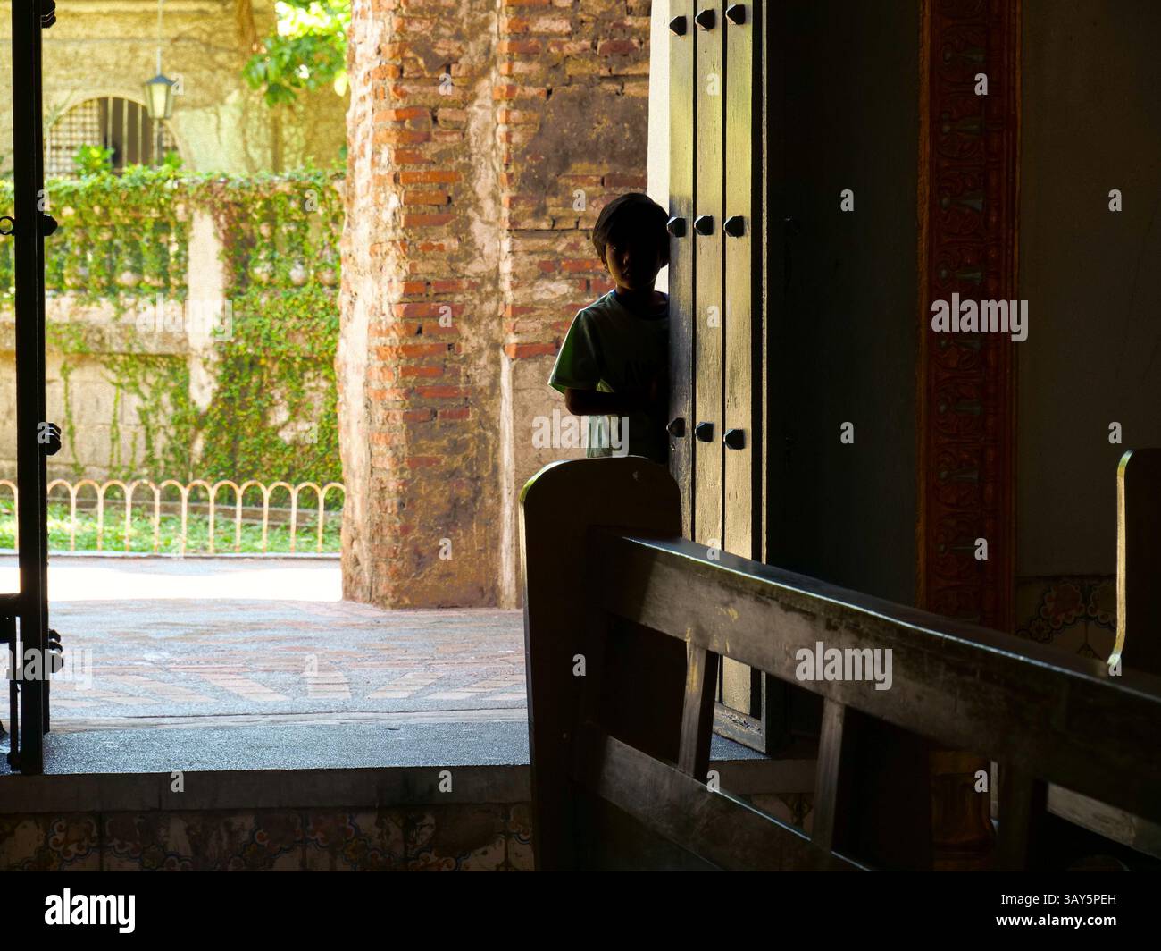 Un individuo si appoggia casualmente contro una porta con una robusta parete in mattoni sullo sfondo, creando un coinvolgente contrasto visivo Foto Stock