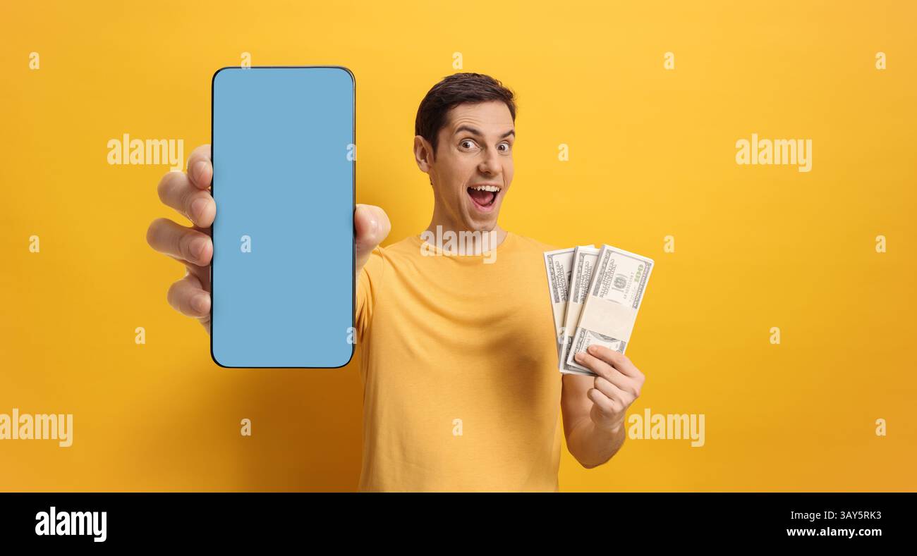 Giovane felice con soldi in mano e smartphone con schermo blu su sfondo giallo Foto Stock