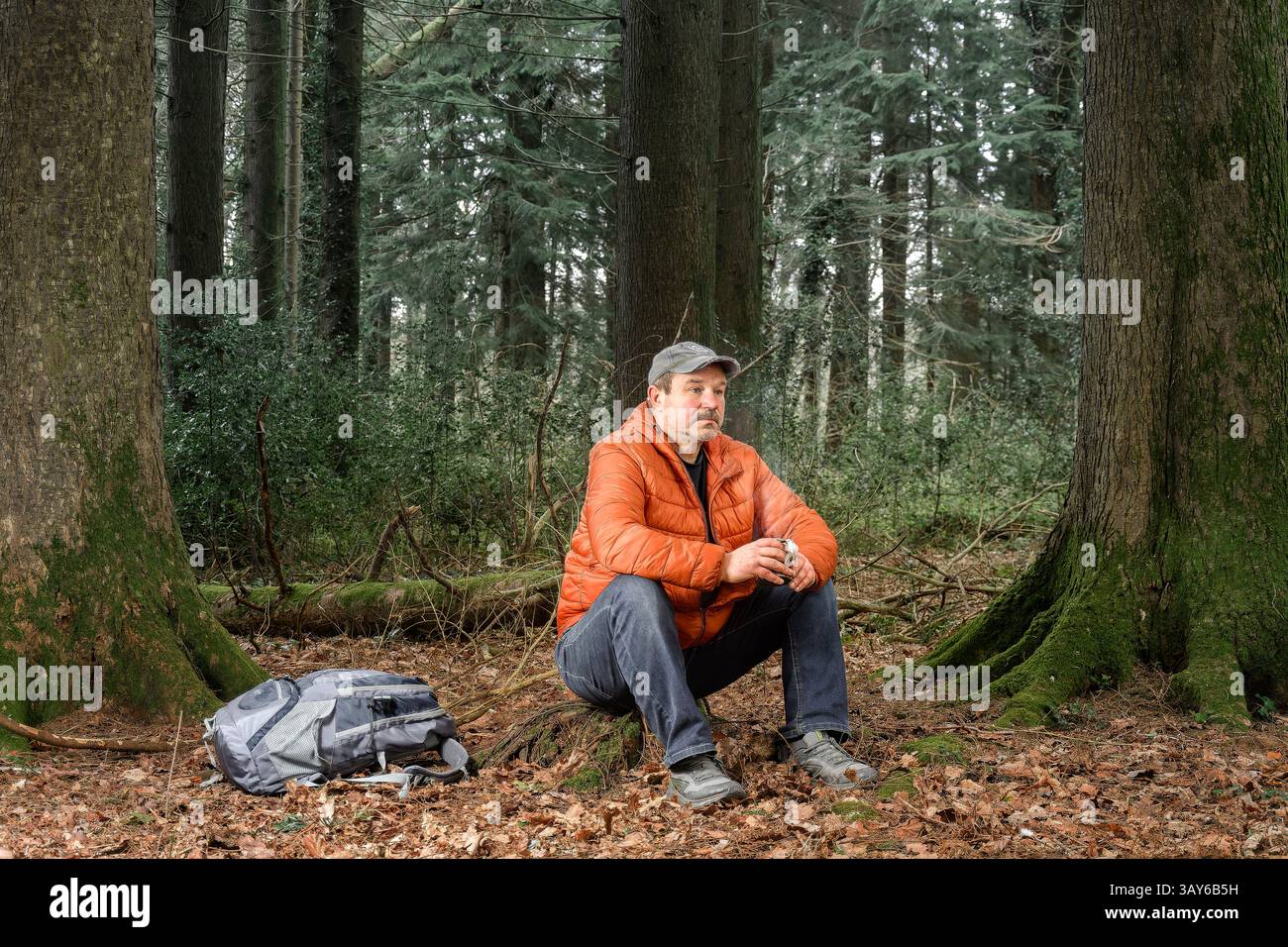 Un uomo si rilassa nella foresta, circondato dalla natura e sorseggia una tazza di bevanda calda, momenti tranquilli nel bosco. Foto Stock