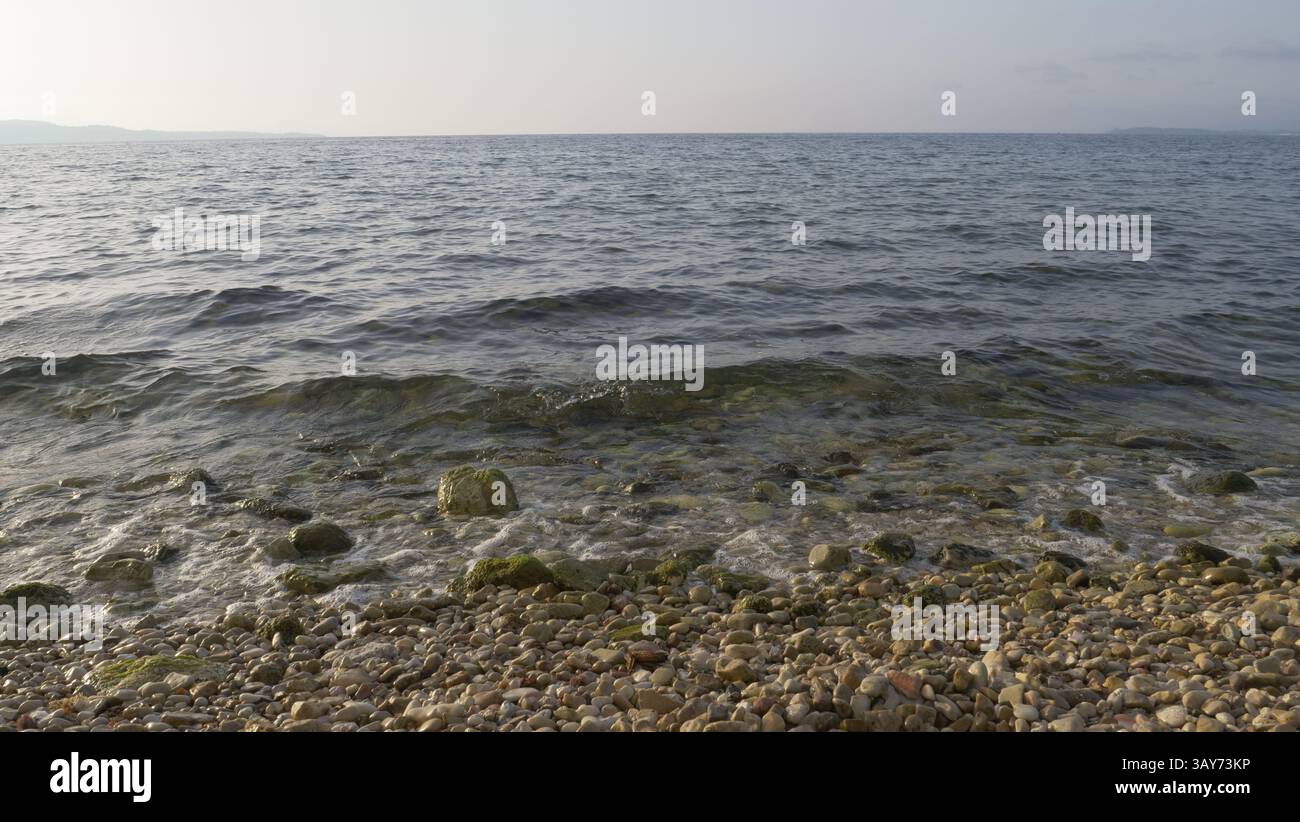 La spiaggia di ciottoli, il mare e l'orizzonte alla spiaggia di Nissaki, Corfù Foto Stock