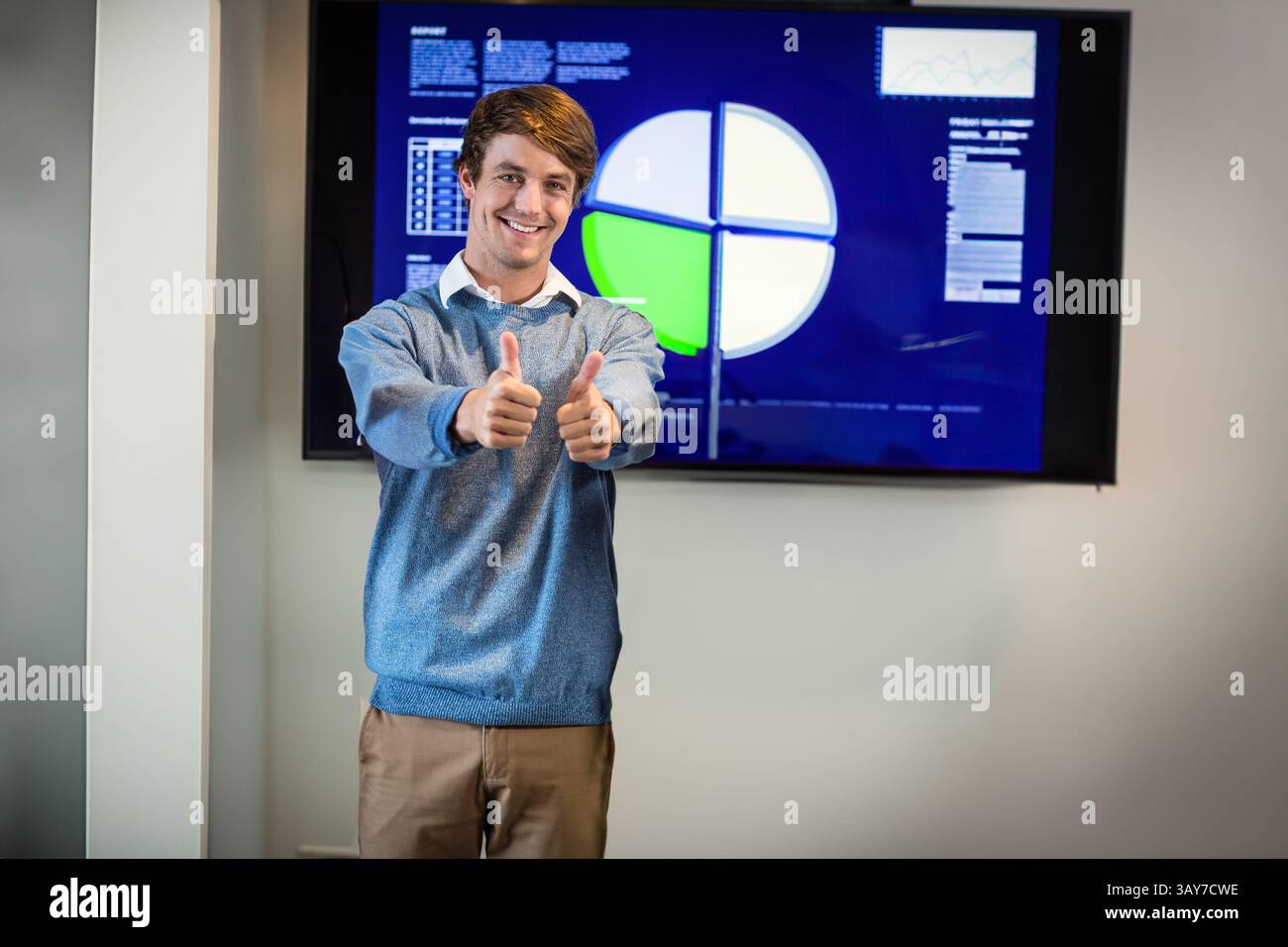 Uomo che regge i pollici in sala conferenze, presenta un grafico a torta su un display montato a parete Foto Stock