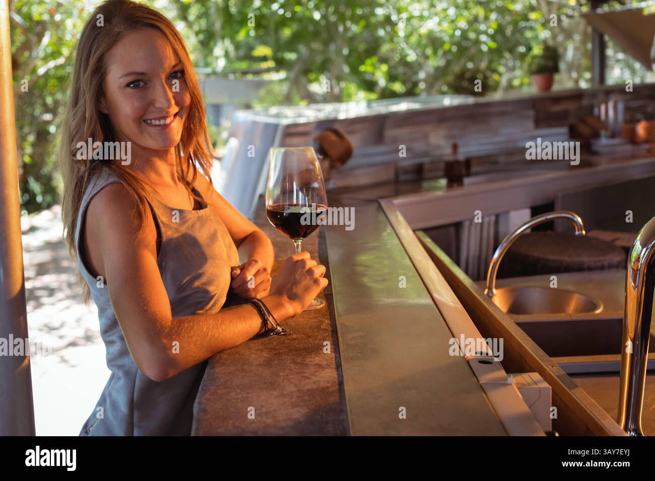 Giovane donna che gusta il vino al bar della cucina all'aperto con piante in vaso e bancone in pietra, spazio fotocopie Foto Stock