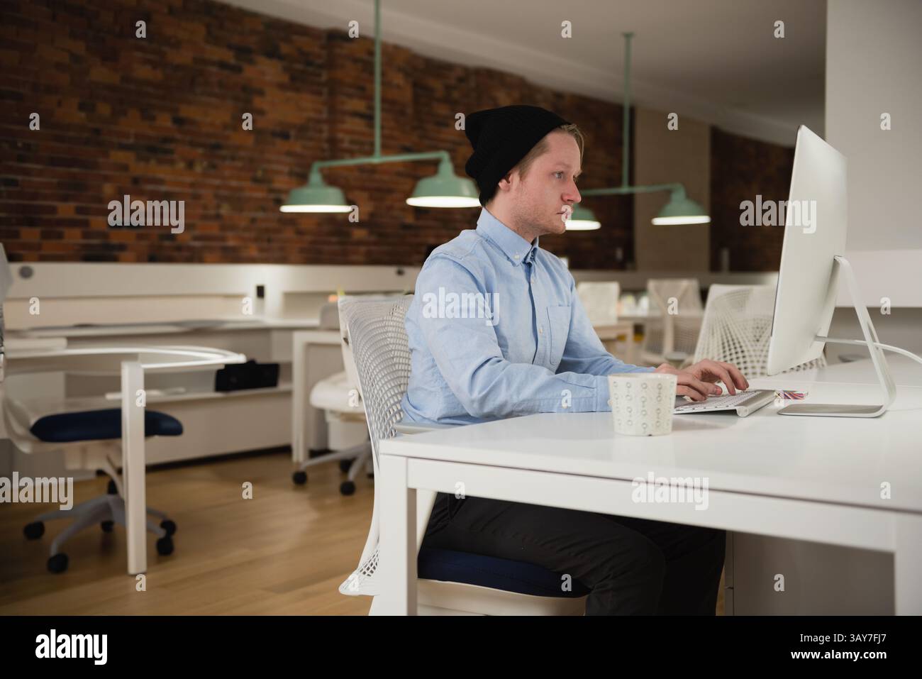 Ragazzo che digita sulla tastiera alla scrivania dell'ufficio con monitor bianco e tazza da caffè, spazio di copia Foto Stock