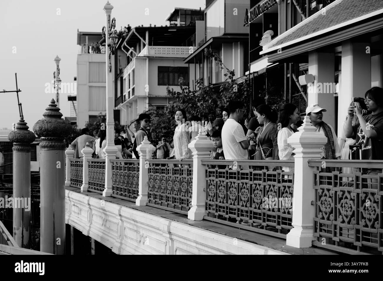 Una folla di visitatori fiancheggia la piattaforma sul lungofiume di fronte al Wat Arun in bianco e nero Foto Stock