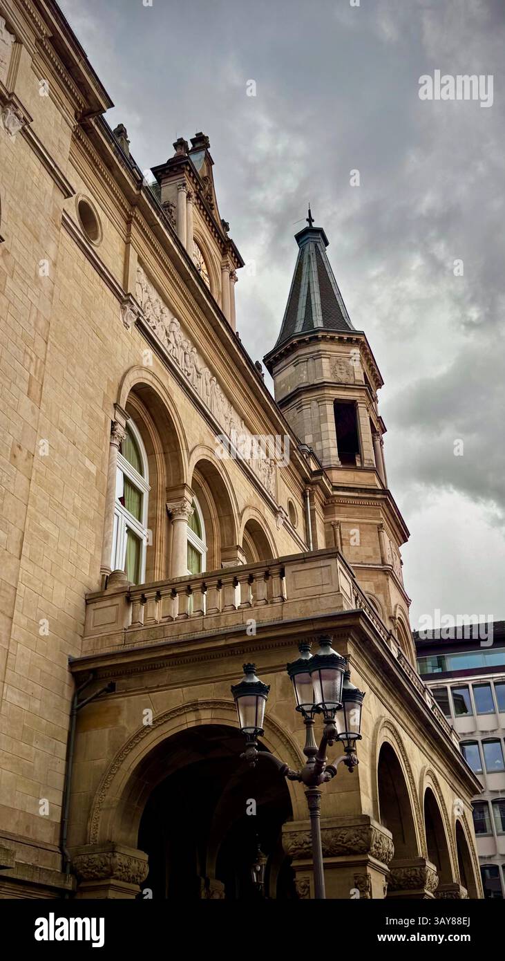 Una vista dettagliata della facciata di un edificio storico e della torre dell'orologio in Lussemburgo, che mostra l'architettura classica e il design decorato sotto un cielo nuvoloso. T - Immagine stock catturata con smartphone