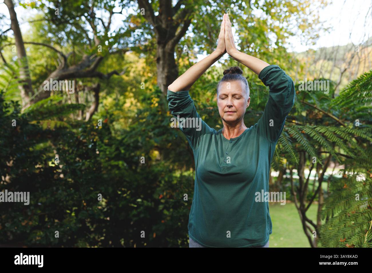 Donna anziana che pratica la preghiera di yoga posa sull'erba nel giardino privato, godendo di momenti tranquilli Foto Stock