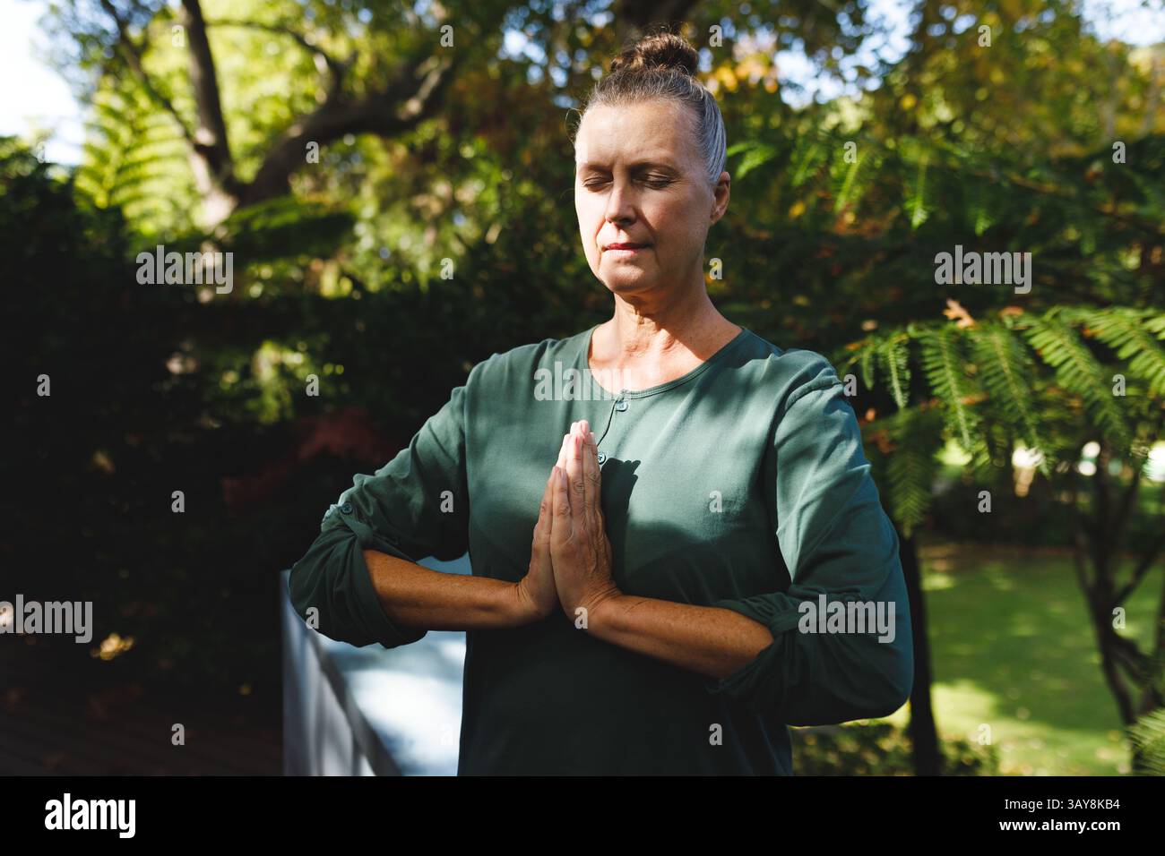 Donna anziana che pratica yoga meditativo posare sul ponte di legno nel giardino sul retro, con divano bianco Foto Stock
