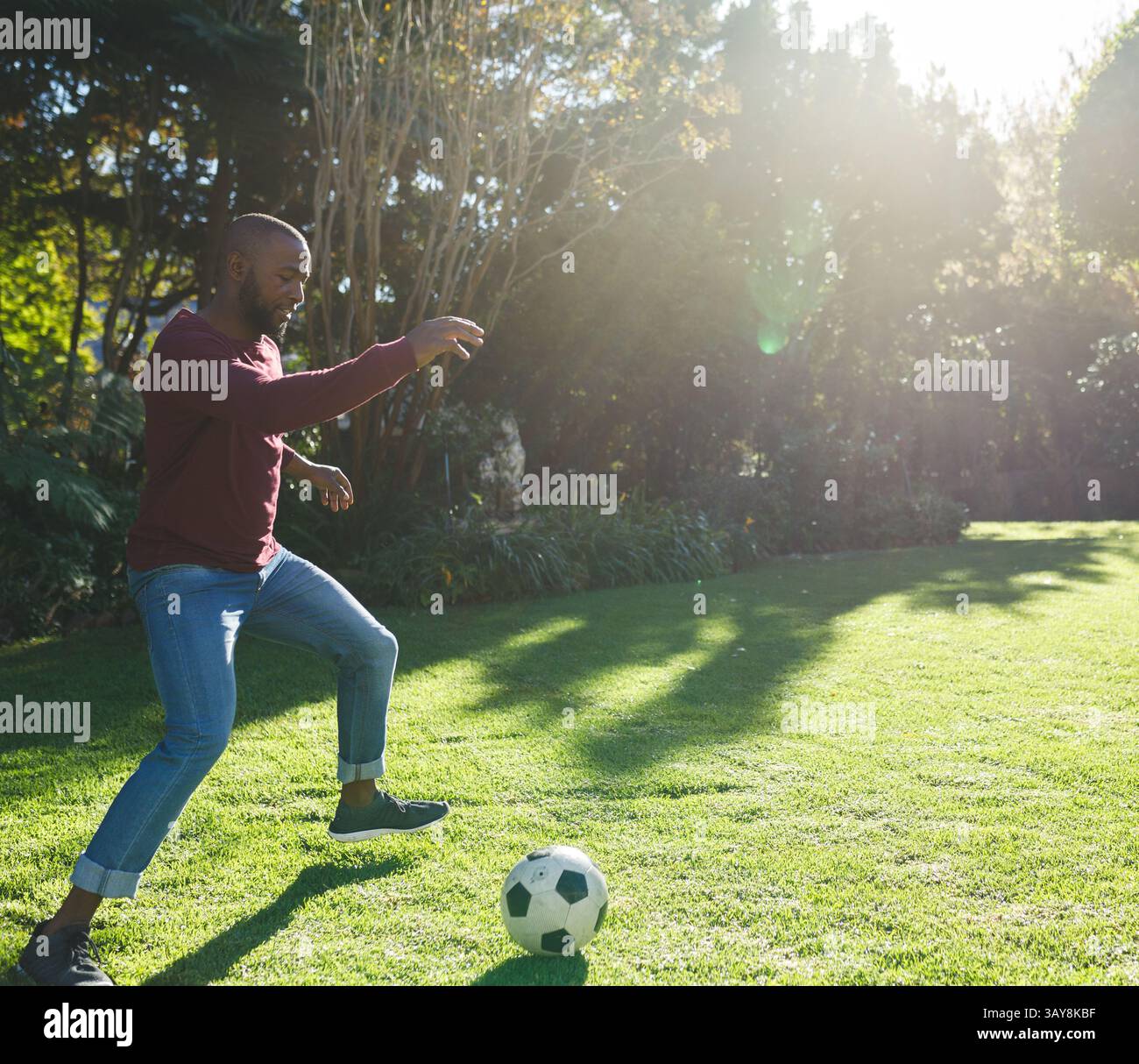Uomo afroamericano maturo che gioca con un pallone da calcio bianco e nero nel giardino privato alla luce del sole Foto Stock