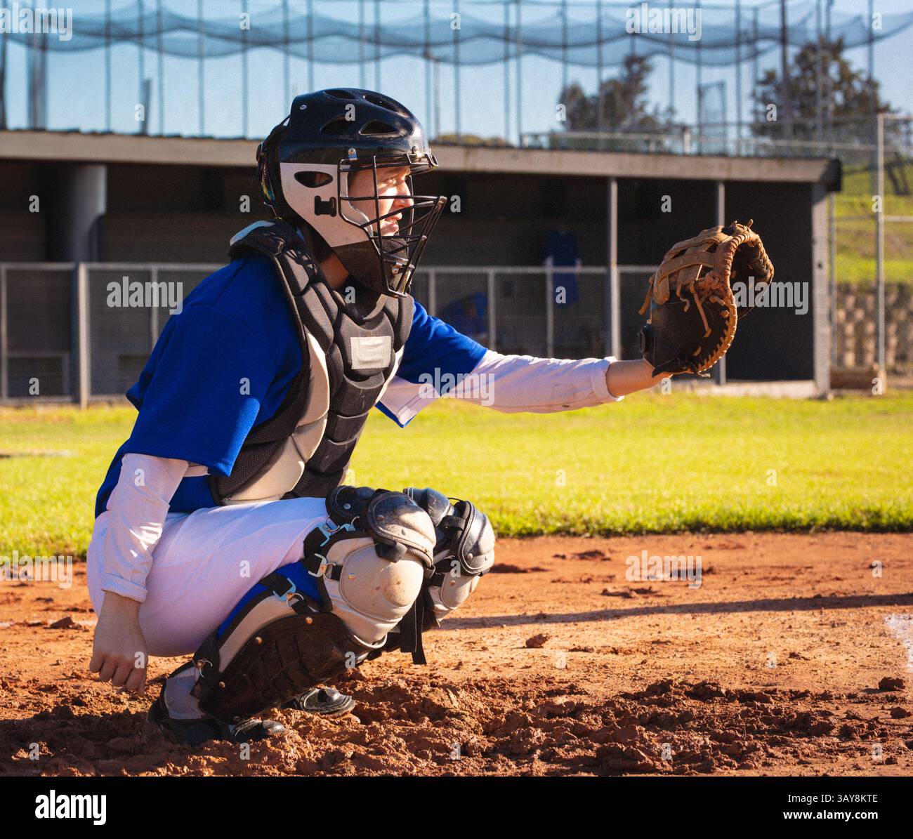 Giovane donna adulta accovacciata sul campo da baseball che tiene il guanto vicino alla recinzione di dugout, spazio per copiare Foto Stock