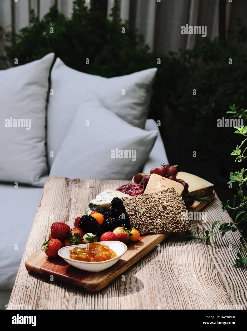 Tagliere di salumi allestito ad arte con una varietà di formaggi, frutta fresca, pane e marmellata, presentati su un rustico tavolo in legno. Foto Stock