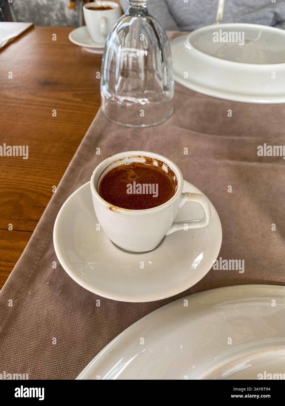 Una tazza di caffè turco appena preparato servito su un piattino bianco su un tavolo di legno con decor neutro. - Immagine stock catturata con smartphone