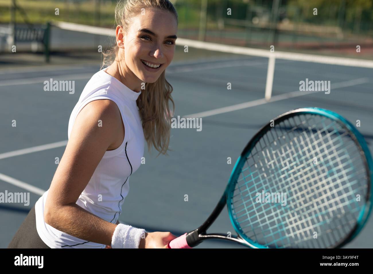 Tennista donna che tiene una racchetta sul campo da tennis all'aperto sorridente alla macchina fotografica e mostra il braccialetto Foto Stock