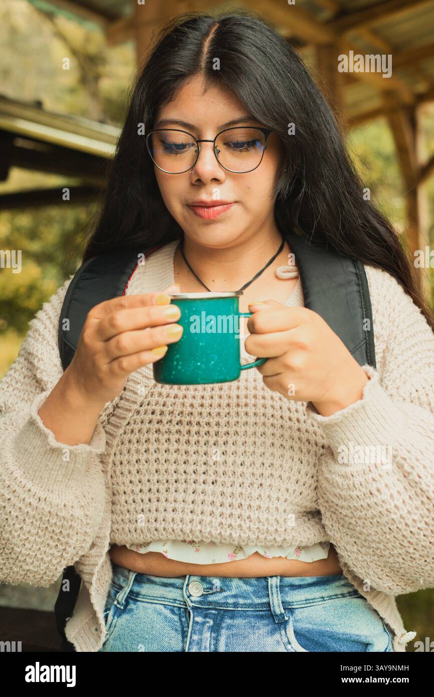 Una giovane donna sta assaporando un momento intimo all'aperto mentre sorseggia il suo delizioso caffè in un elegante maglione in maglia Foto Stock