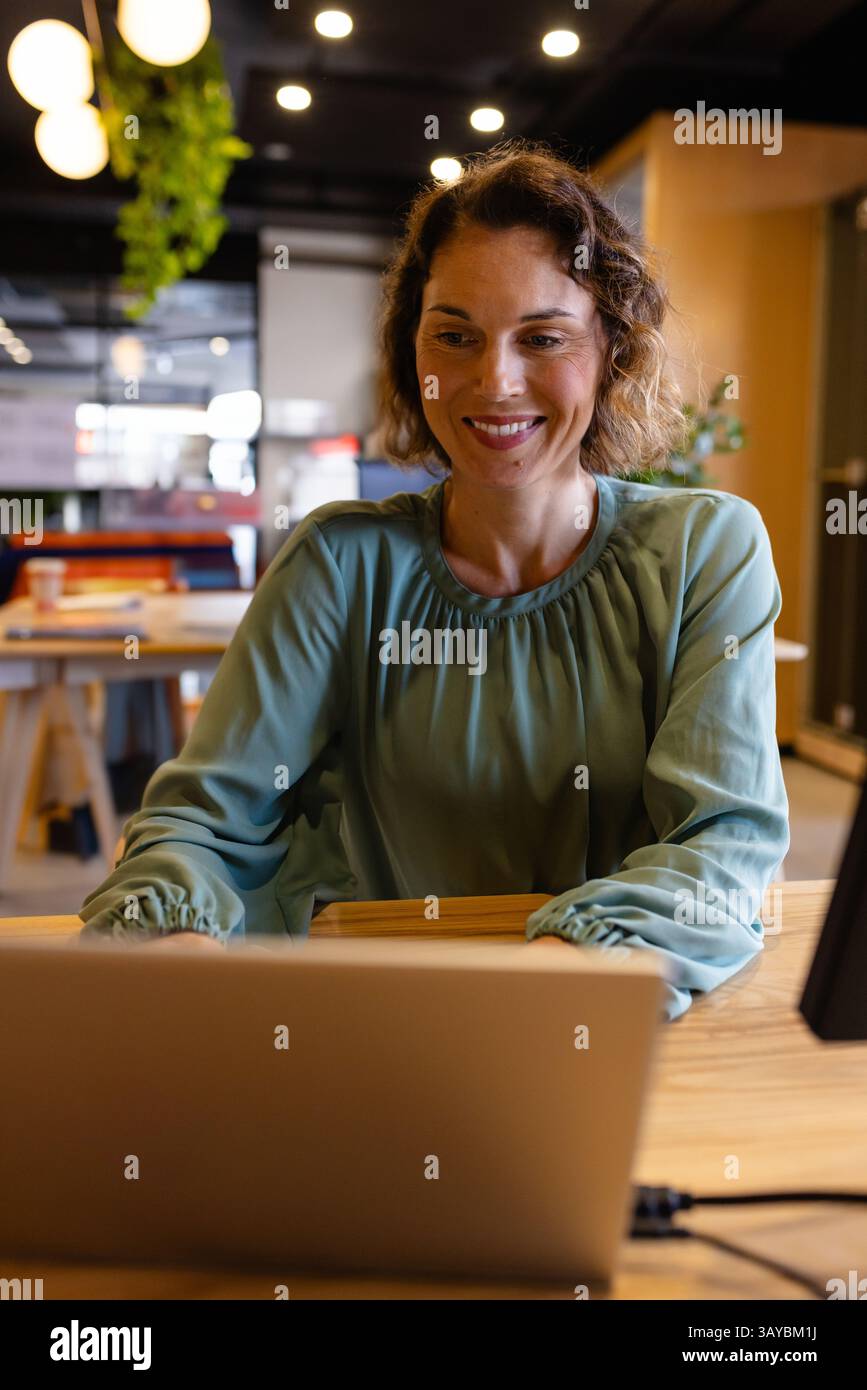 Donna all'inizio degli anni '40 che scrive su un notebook in un ufficio open space, con piante e luci Foto Stock
