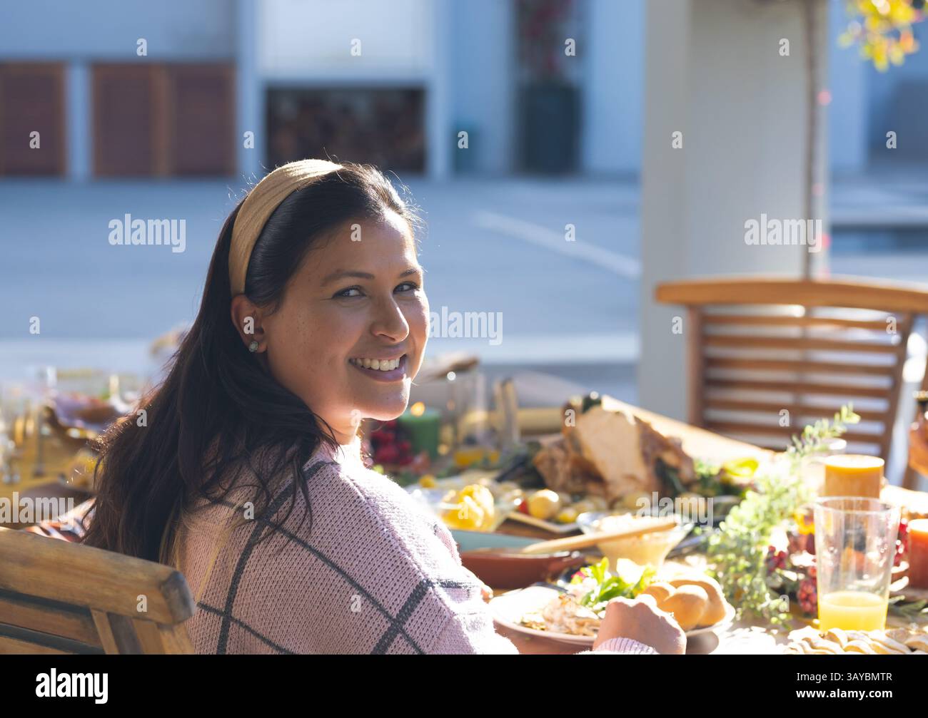 Donna che gira e sorride verso la macchina fotografica al tavolo del patio all'aperto, con tacchino arrosto e panini Foto Stock