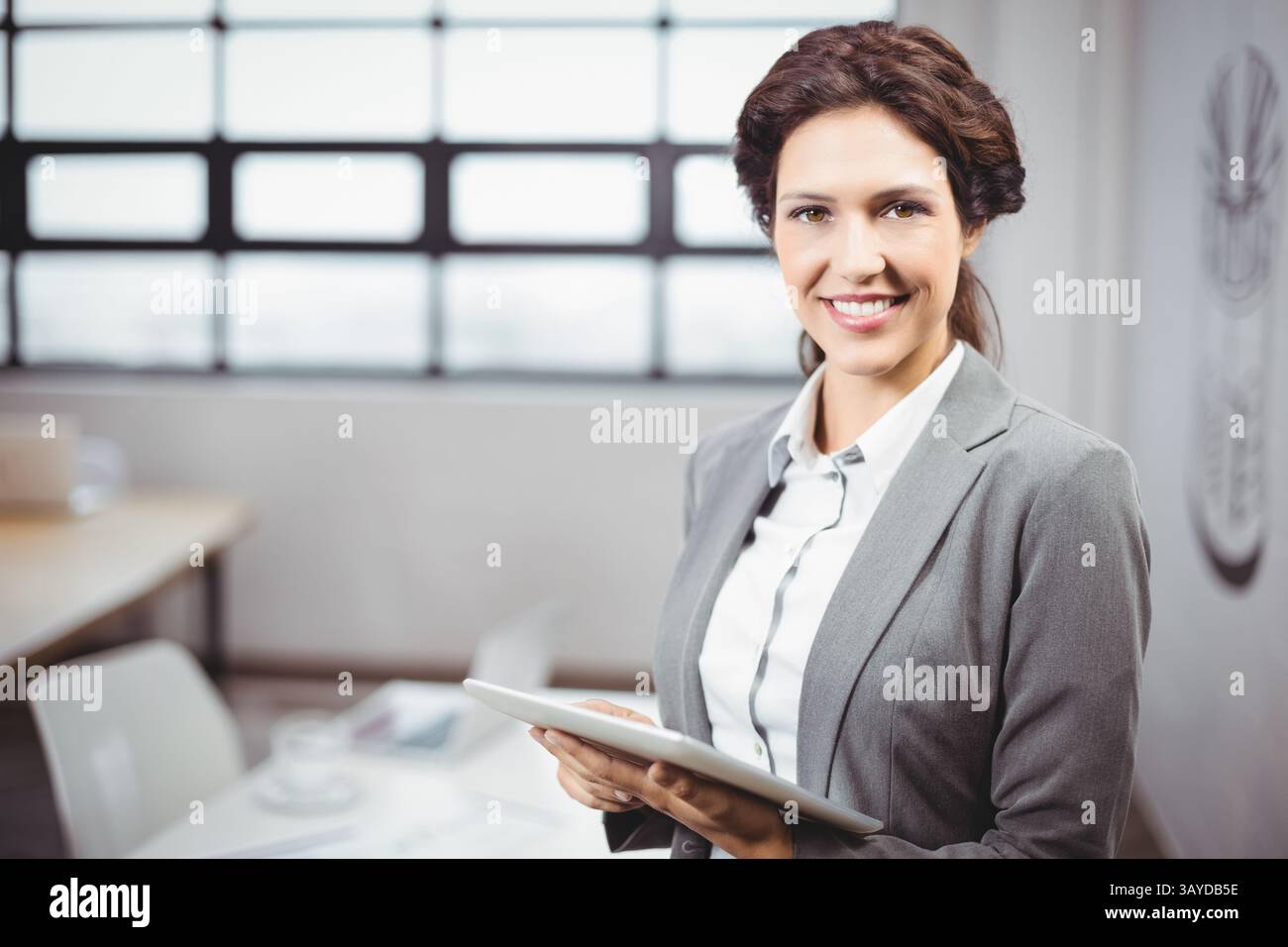 Donna d'affari che sorride e tiene un tablet nella sala conferenze vicino a un tavolo con una tazza di caffè e uno spazio fotocopie Foto Stock