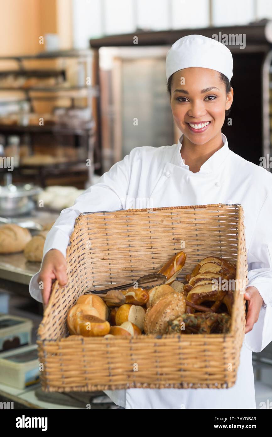 panettiera afroamericana in piedi nel panificio con cesto di vimini di pane e dolci, sorridente Foto Stock