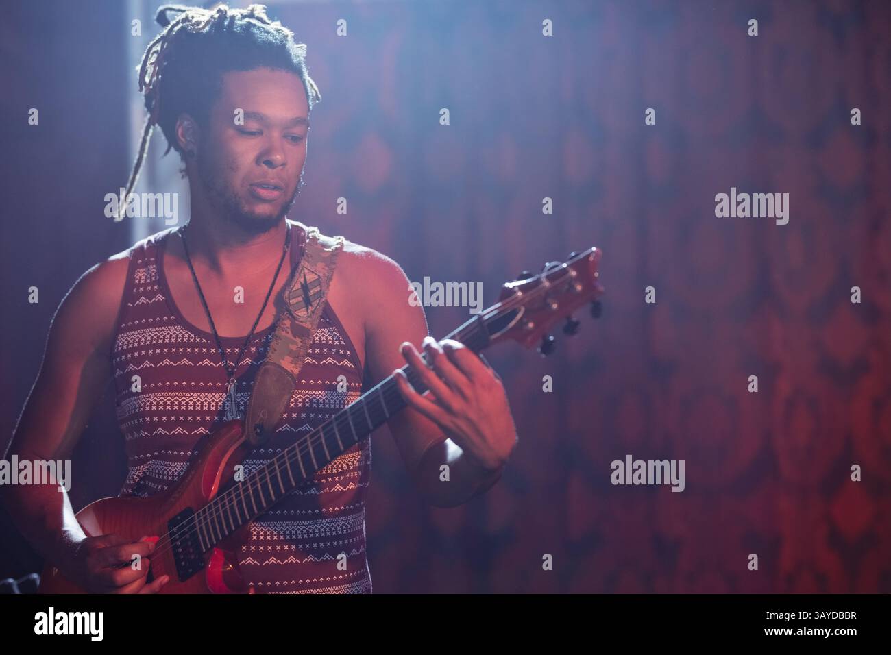 Musicista maschile che suona la chitarra elettrica sul palco fibroso sotto luci colorate, con cinturino decorato Foto Stock