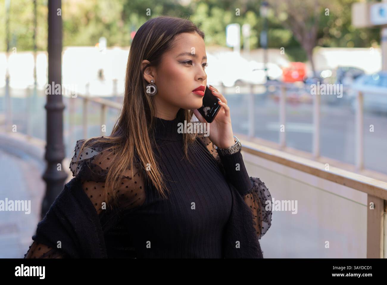 Una donna elegante che fa una telefonata, vestita con un abito nero alla moda, scattata in un ambiente urbano. Foto Stock
