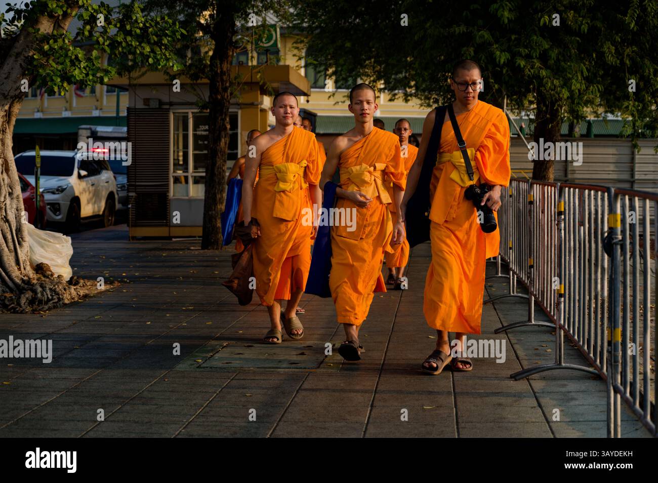I monaci con le vivaci vesti arancioni camminano per la città all'ora d'oro, uno con una macchina fotografica Foto Stock