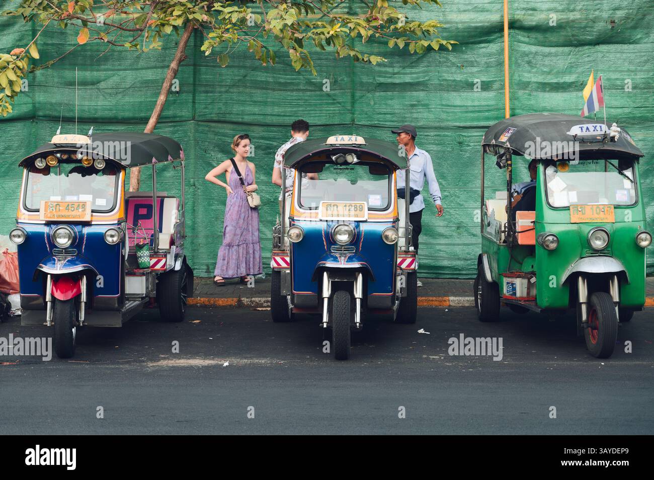 I turisti chiacchierano con un autista accanto a una fila di tuk-tuk colorati Foto Stock