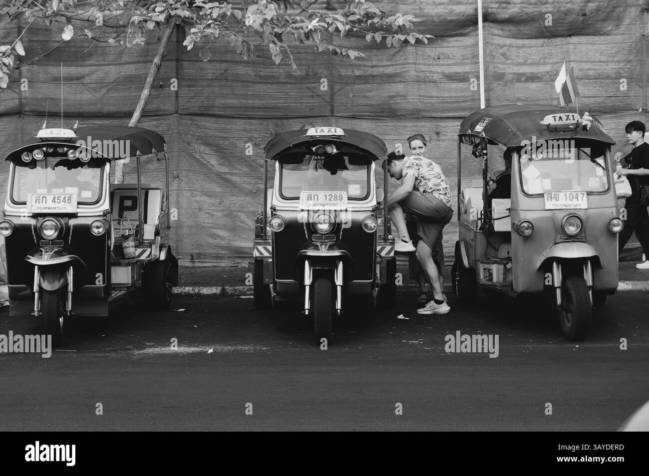 Una coppia di turisti si arrampica in un tuk-tuk, fiancheggiato da una fila di iconici taxi a tre ruote Foto Stock