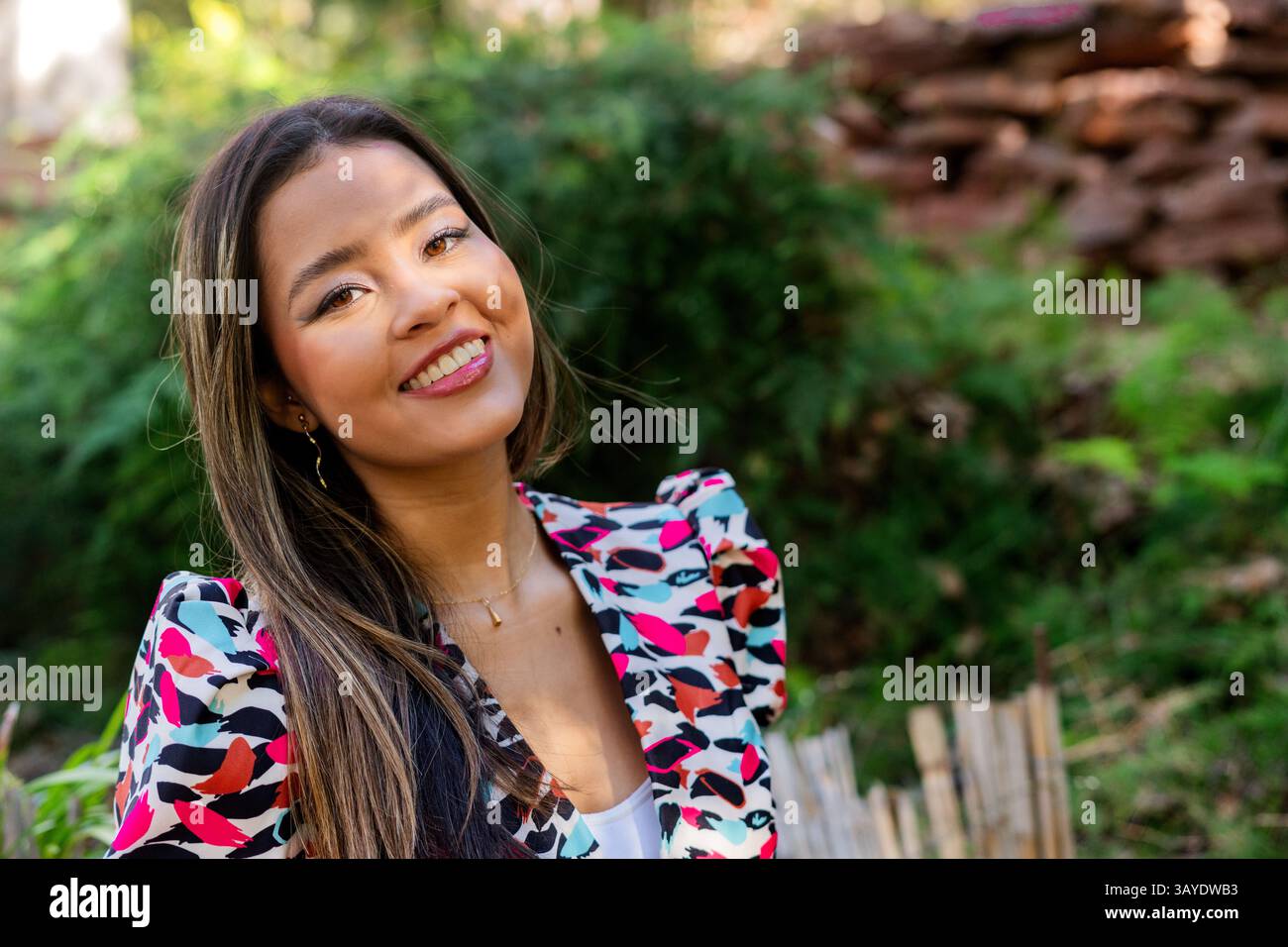 Una giovane e allegra donna posa felicemente all'aperto, mostrando il suo abbigliamento luminoso e vibrante in mezzo alla lussureggiante vegetazione Foto Stock
