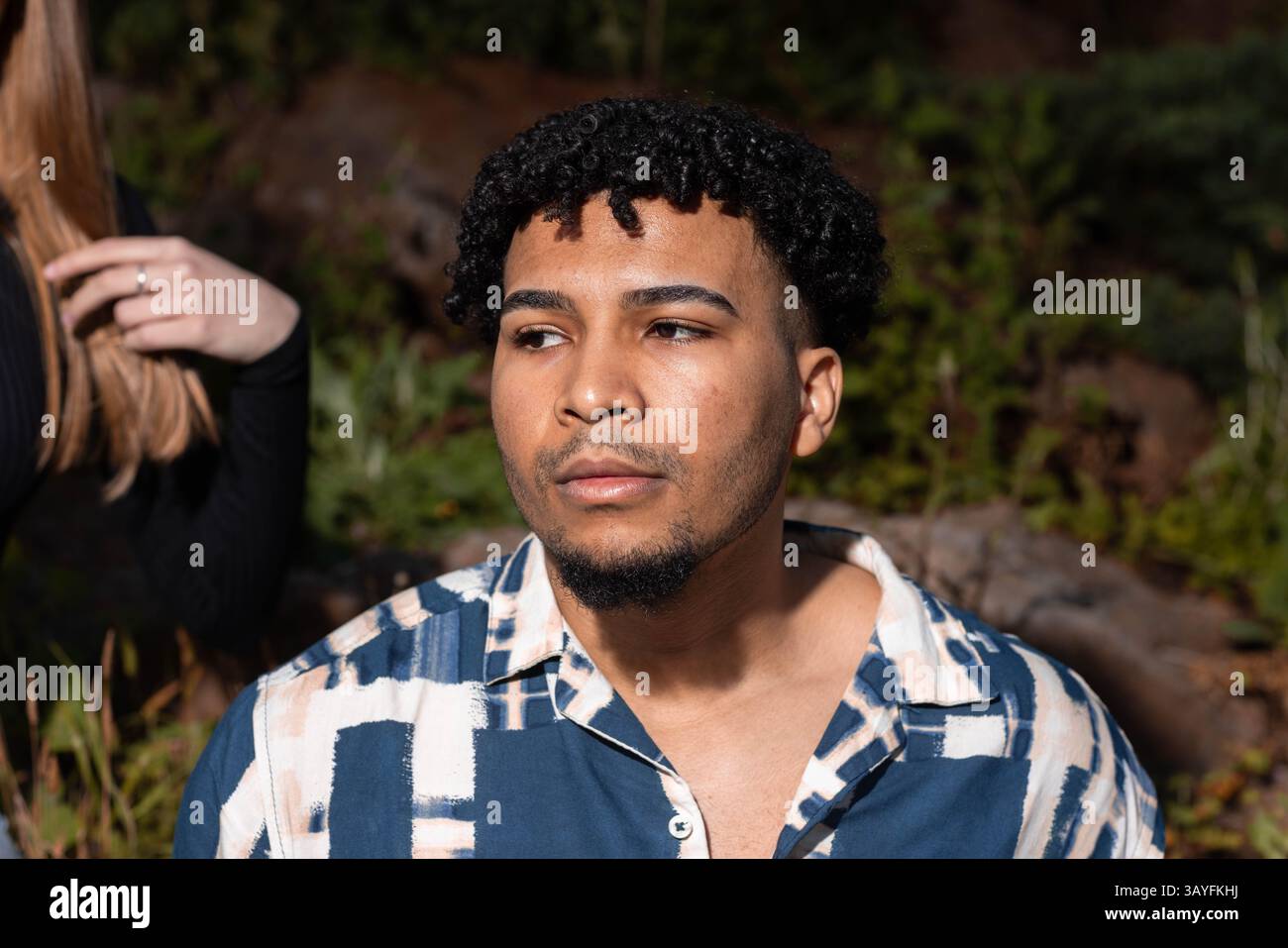 Primo piano Ritratto di un giovane uomo elegante con capelli ricci in un ambiente naturale all'aperto Foto Stock