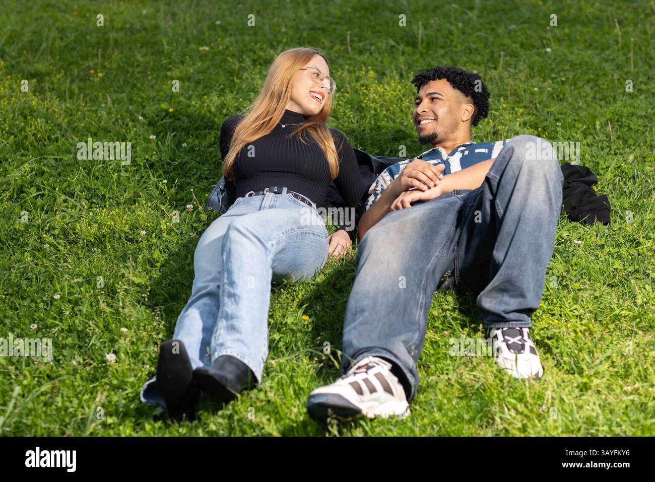 Giovane coppia sdraiata su erba sorridente l'una all'altra a Urban Park Foto Stock