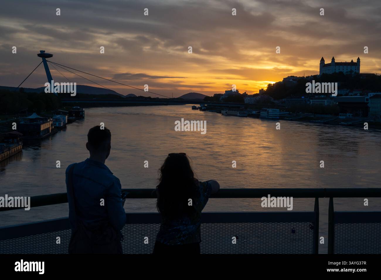 Bratislava, Slovacchia. 20 aprile 2025. Giovani coppie osservano il tramonto sul Danubio nella capitale slovacca Bratislava. Sullo sfondo si trovano la torre UFO, il ponte SNP, il castello di Bratislava e la cattedrale di San Martino. (Immagine di credito: © Tomas Tkacik/SOPA Images via ZUMA Press Wire) SOLO PER USO EDITORIALE! Non per USO commerciale! Foto Stock