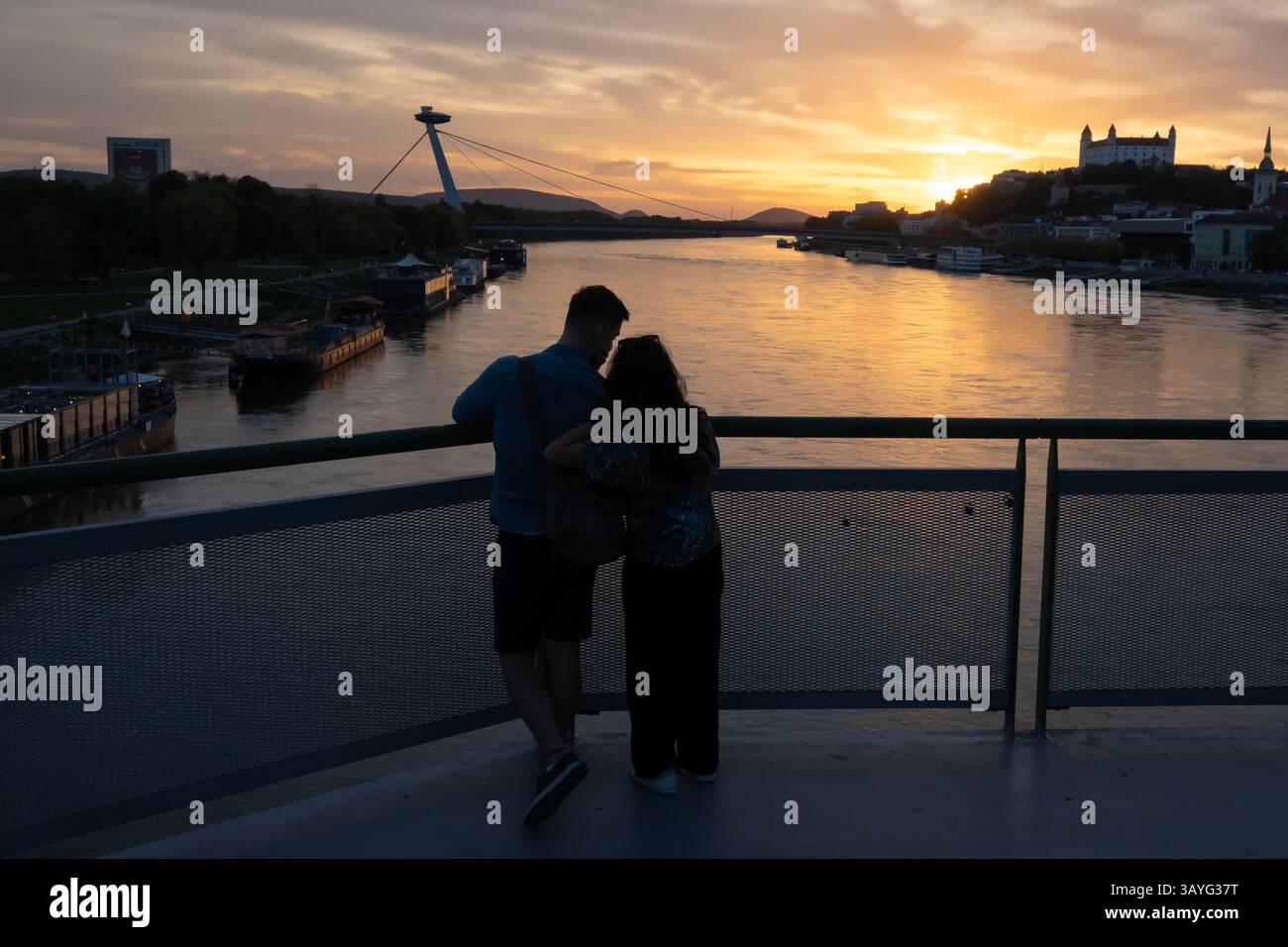 Bratislava, Slovacchia. 20 aprile 2025. Giovani coppie osservano il tramonto sul Danubio nella capitale slovacca Bratislava. Sullo sfondo si trovano la torre UFO, il ponte SNP, il castello di Bratislava e la cattedrale di San Martino. (Immagine di credito: © Tomas Tkacik/SOPA Images via ZUMA Press Wire) SOLO PER USO EDITORIALE! Non per USO commerciale! Foto Stock