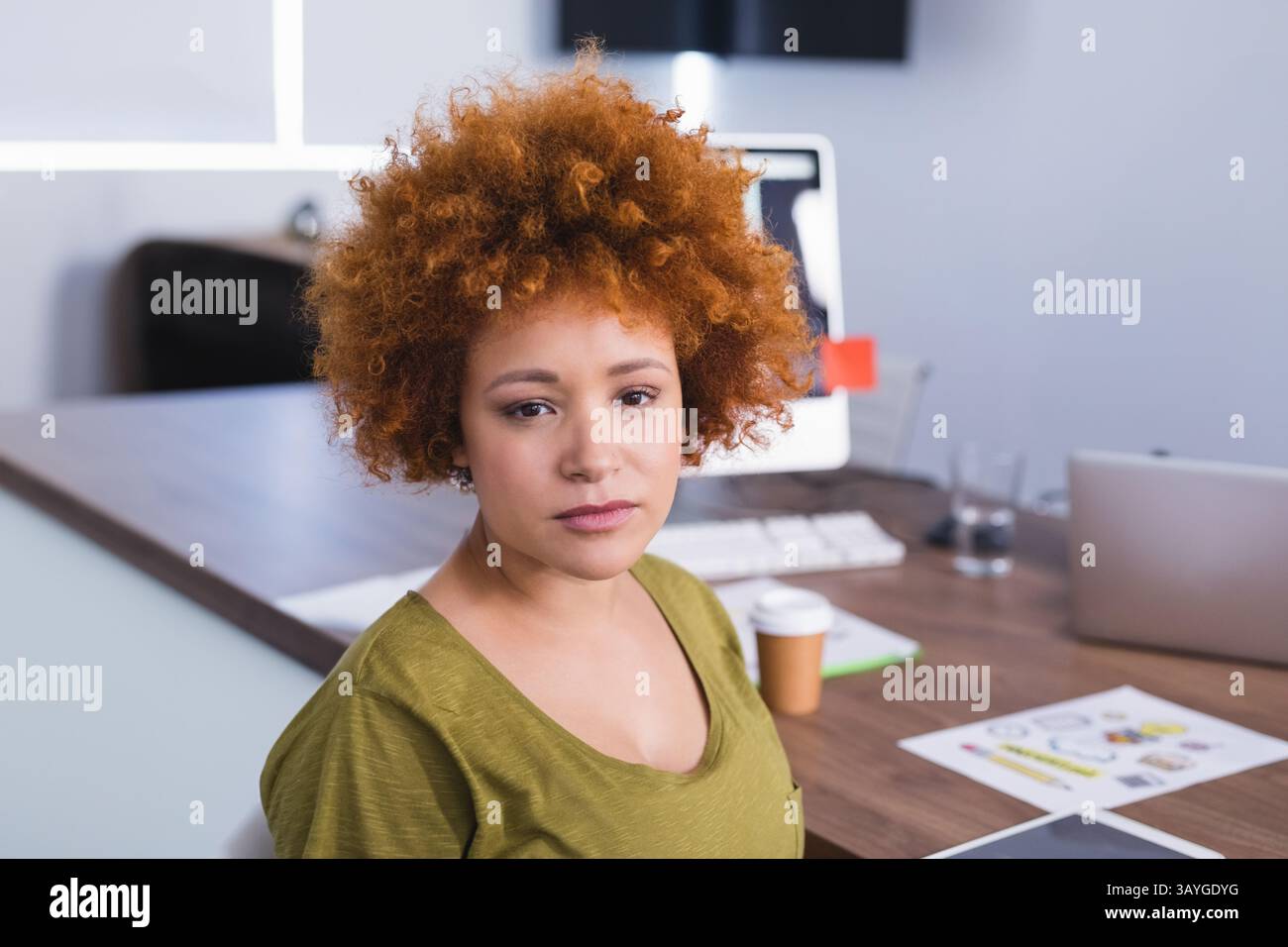 Donna che lavora su computer e laptop in un ufficio moderno con carte, tazza da caffè e bicchieri d'acqua Foto Stock