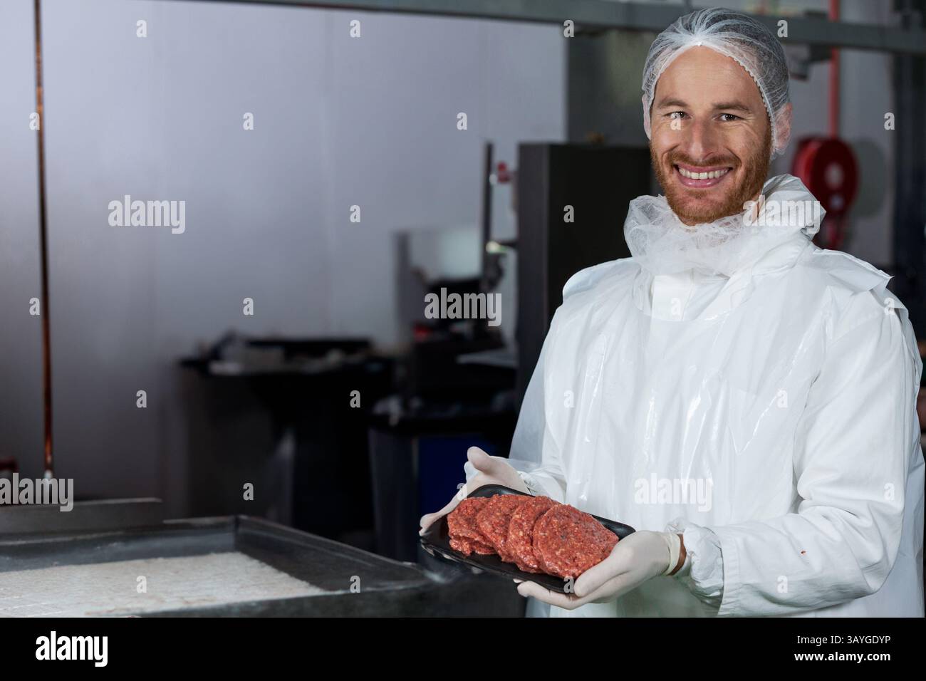 Uomo che posiziona un vassoio nero di polpette di hamburger crude su un tavolo in acciaio inossidabile all'interno dell'impianto di lavorazione della carne Foto Stock