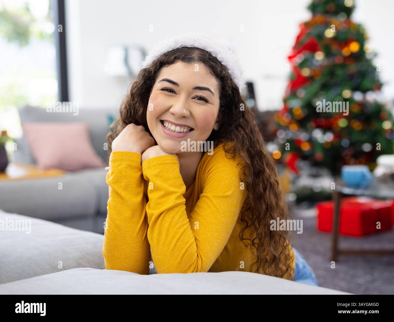 Giovane donna adulta appoggiata sul divano nel soggiorno con decorazioni natalizie, albero, cuscini e fascia Foto Stock