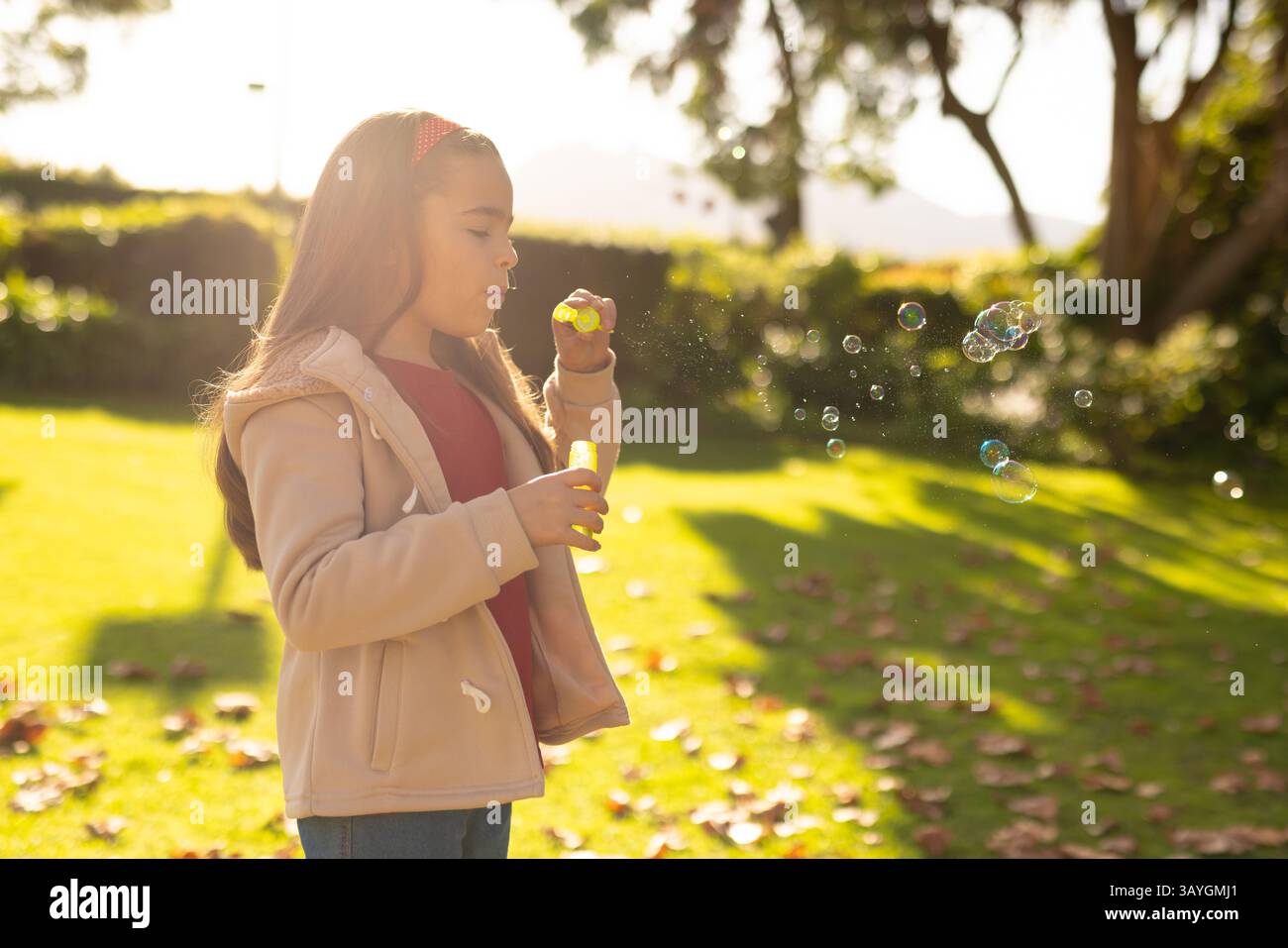 bambina di 6 anni che soffia bolle di sapone in giardino, con bacchetta gialla e bottiglia di soluzione, spazio copia Foto Stock