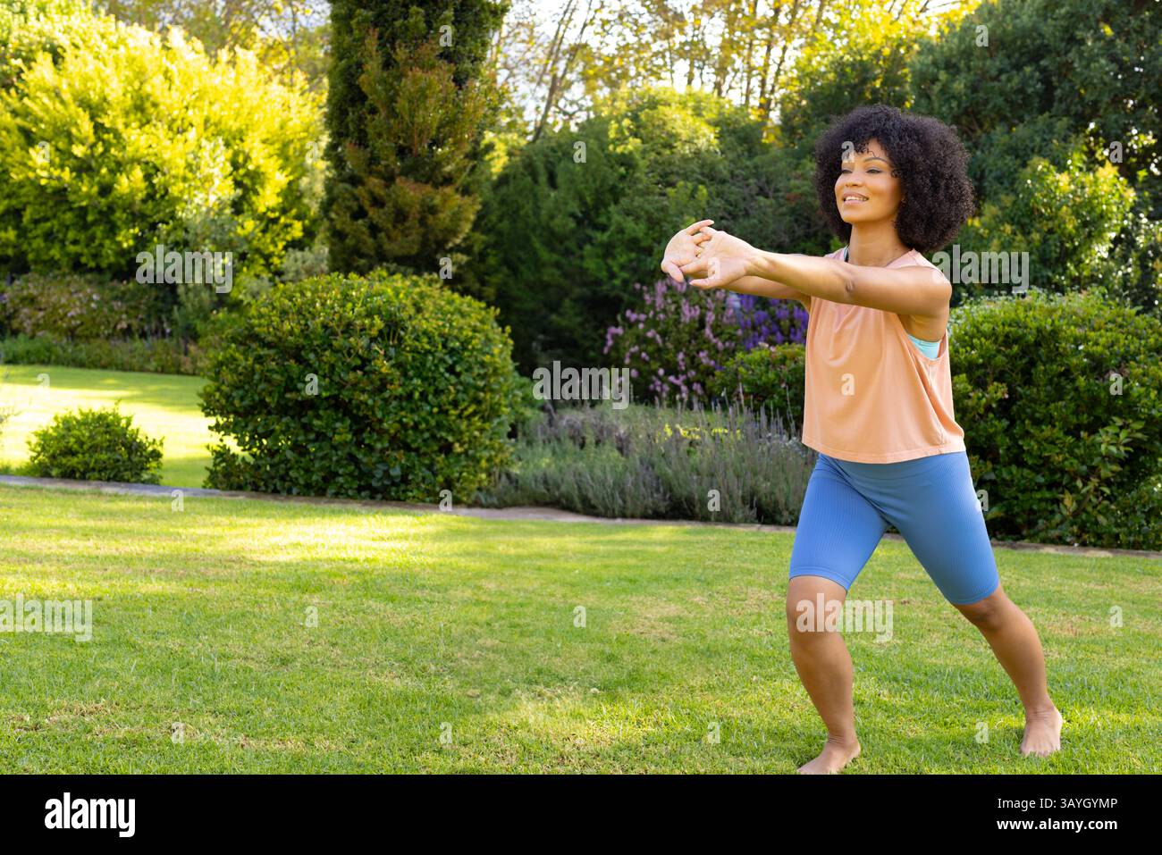 Donna che esegue affondo si estende nel giardino privato del cortile, con arbusti fioriti, spazio copia Foto Stock