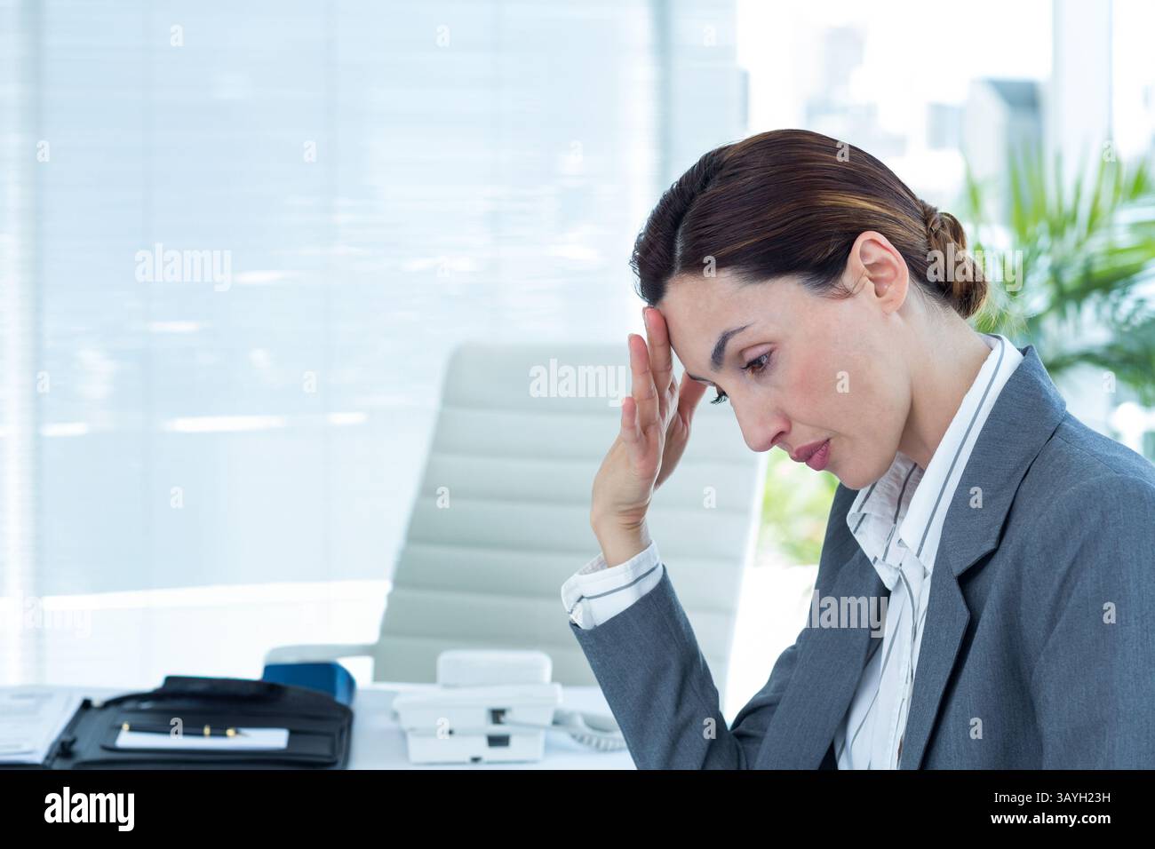 Donna d'affari di medie dimensioni seduta alla scrivania, con la testa appoggiata a mano con telefono, documenti, spazio fotocopie Foto Stock