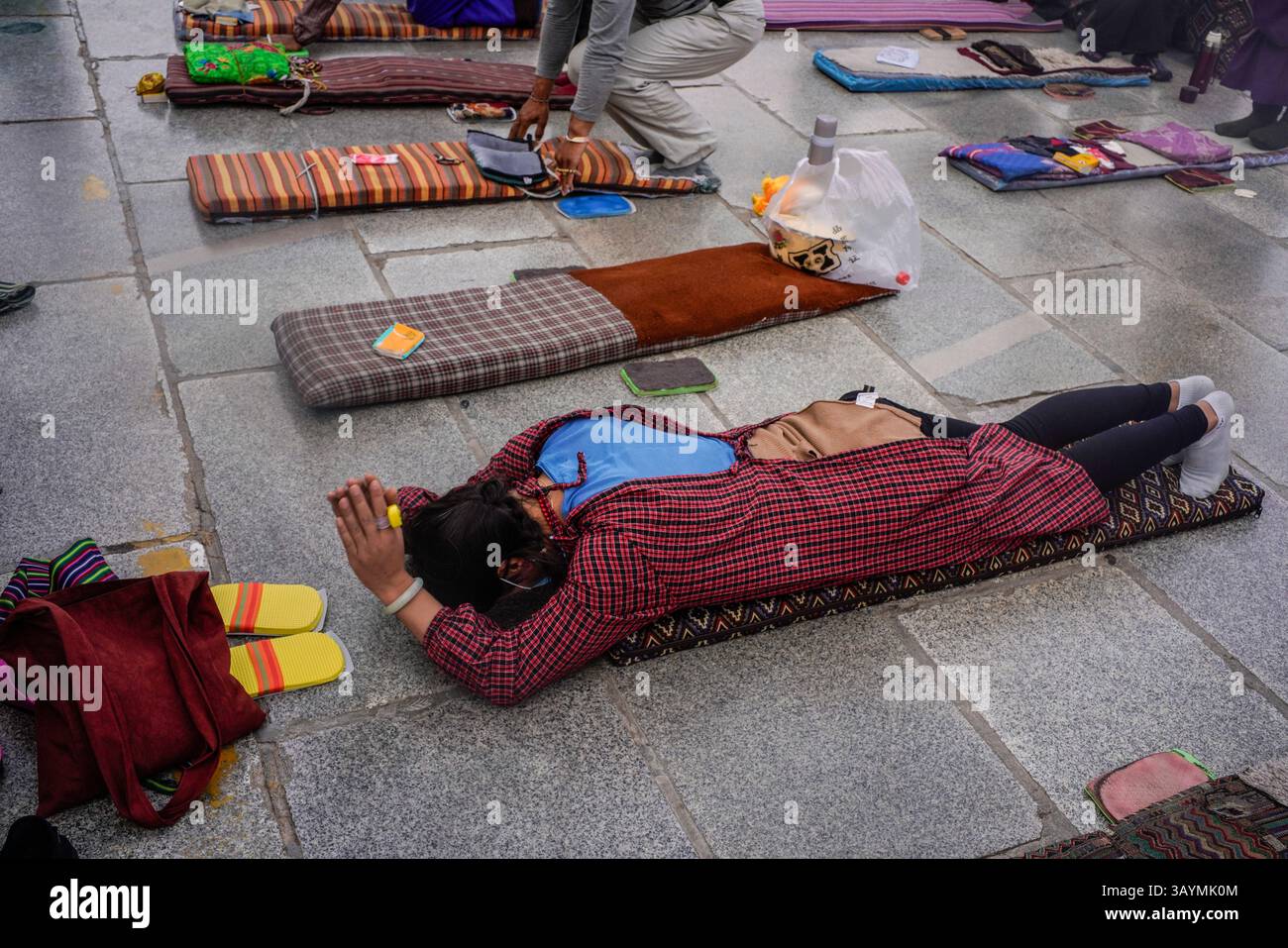 Nel cuore della città vecchia di Lhasa, i pellegrini tibetani si esibiscono prostrazioni a tutto corpo prima del sacro Tempio di Jokhang. Questo antico atto di de Foto Stock