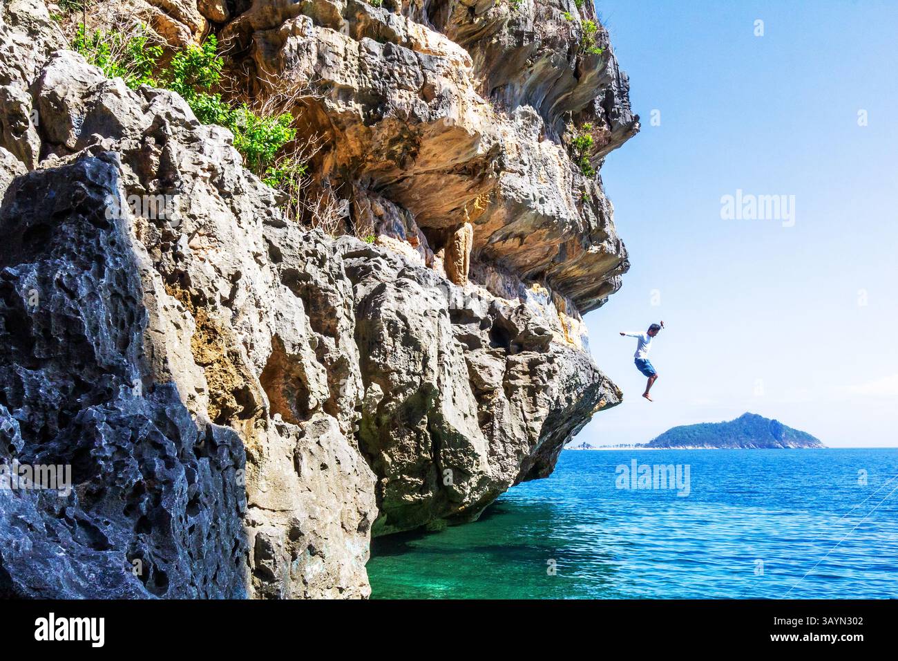 Un locale filippino salta da una scogliera rocciosa nel vivace mare blu di Isla de Gigantes a Iloilo, Filippine Foto Stock