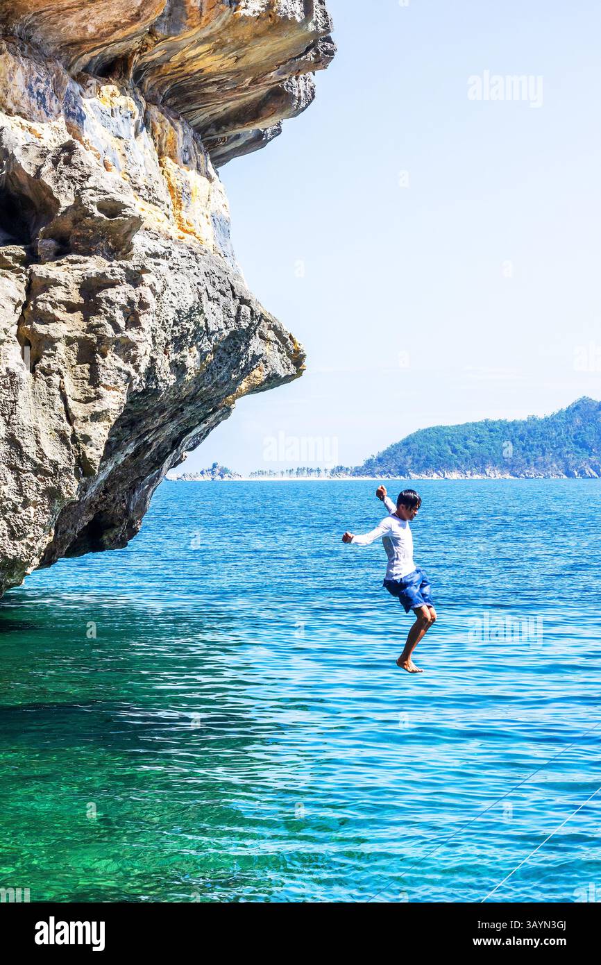 Un locale filippino salta da una scogliera rocciosa nel vivace mare blu di Isla de Gigantes a Iloilo, Filippine Foto Stock