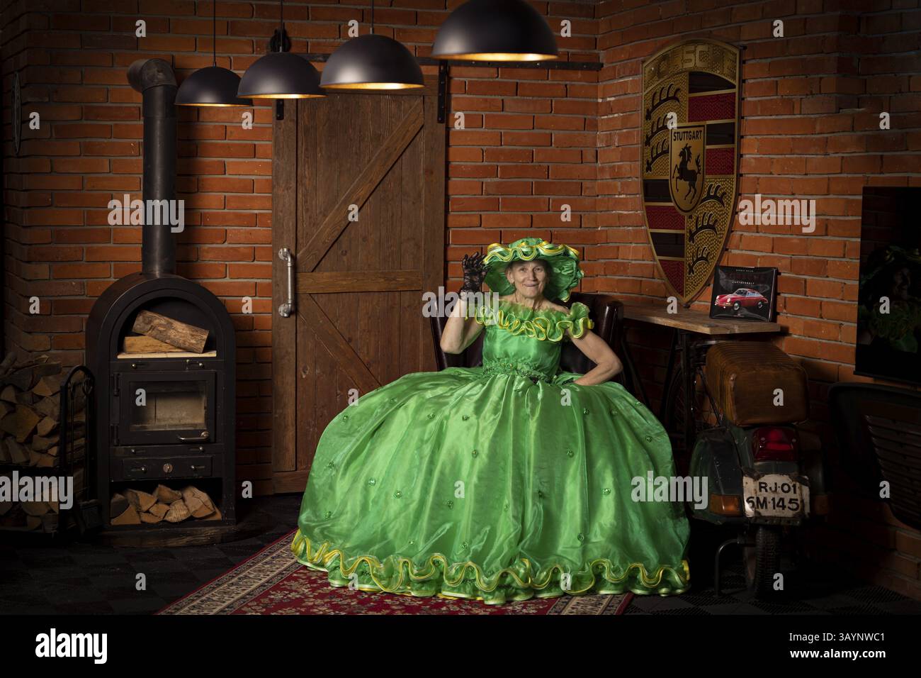 Donna in abito verde seduta in una stanza rustica con caminetto e pannelli in legno, servizio fotografico in scena, Mindelheim, Unterallgaeu, Baviera, Germania, Europ Foto Stock