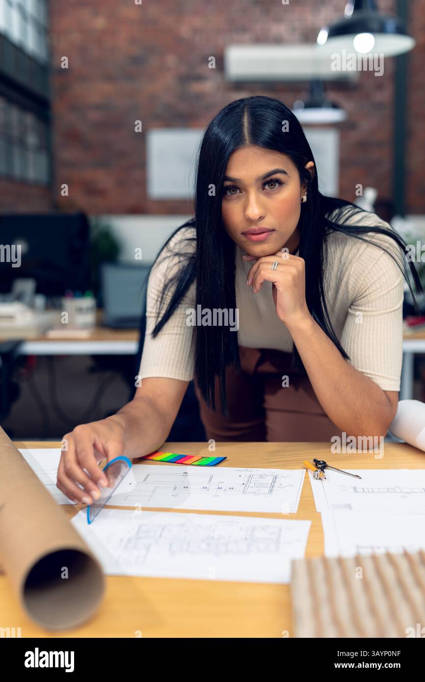 Architetto donna che rivede i progetti sul tavolo nello studio di progettazione, con campione di colore e quadrato Foto Stock