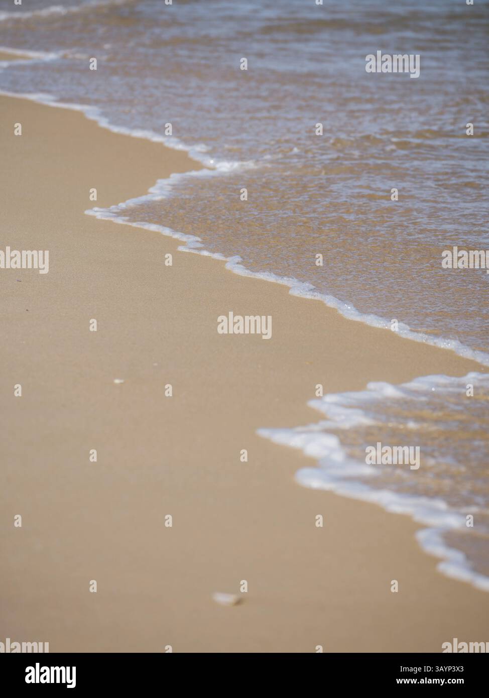 Faro, Algarve, Portogallo, primo piano di piccole onde che colpiscono la riva di una spiaggia sabbiosa, l'Europa Foto Stock