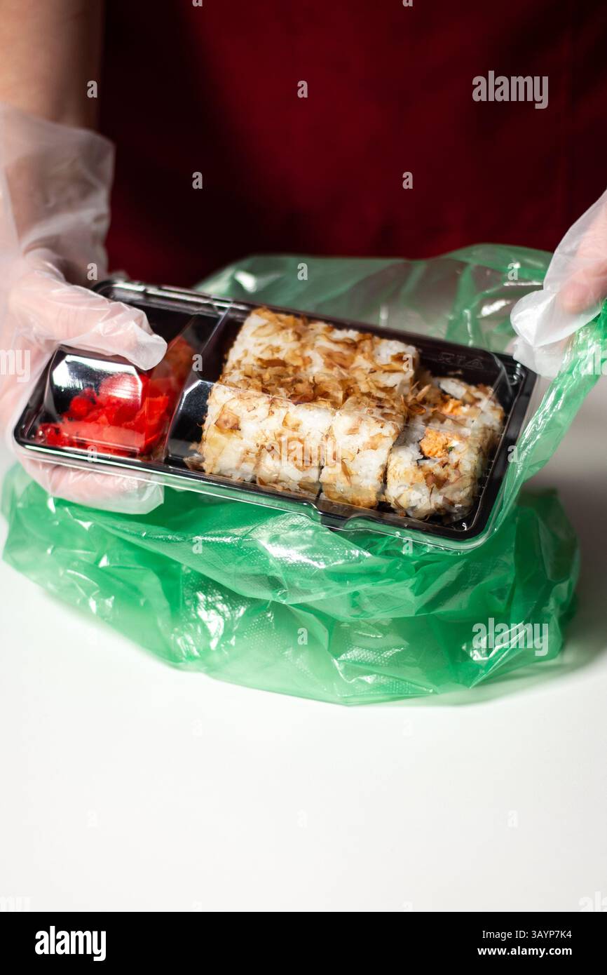 Concetto di sushi To Go. Scatola da asporto con rotoli di sushi in mani da donna e guanti. Concetto di consegna del cibo. Concetto di cibo da asporto. Foto Stock