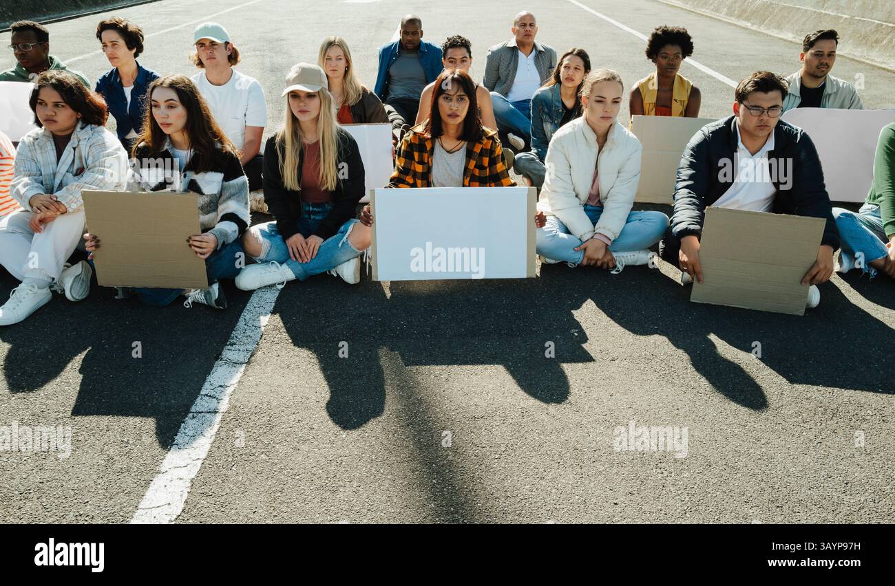 Un gruppo diversificato di individui si riunì all'aperto, dimostrando con cartelli bianchi mentre si sedeva in una strada della città. Questa scena rappresenta l'attivismo, solida Foto Stock