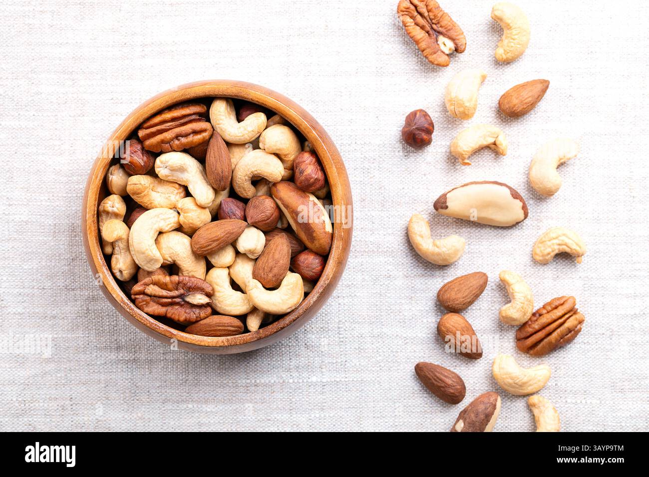 Mix di noci arrostite, snack in una ciotola di legno su lino. Miscela di anacardi arrostiti, mandorle, nocciole, noci del Brasile e noci pecan. Foto Stock
