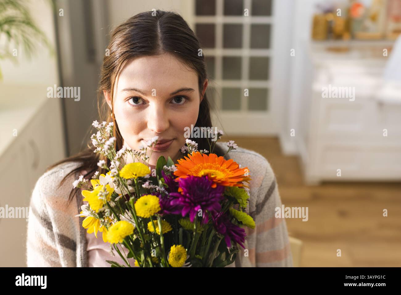 Donna che tiene in mano un vivace bouquet di fiori misti nel soggiorno, con margherite arancioni e mamme Foto Stock