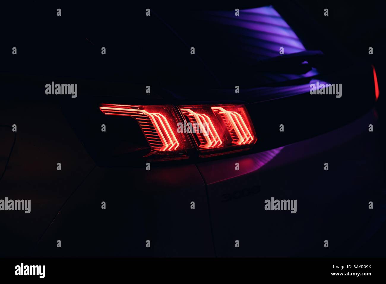 Luce di coda di un'auto moderna di notte. Immagine ravvicinata della luce posteriore a LED con tre strisce, linee al neon viola che si riflettono sulla carrozzeria dell'auto. Foto Stock