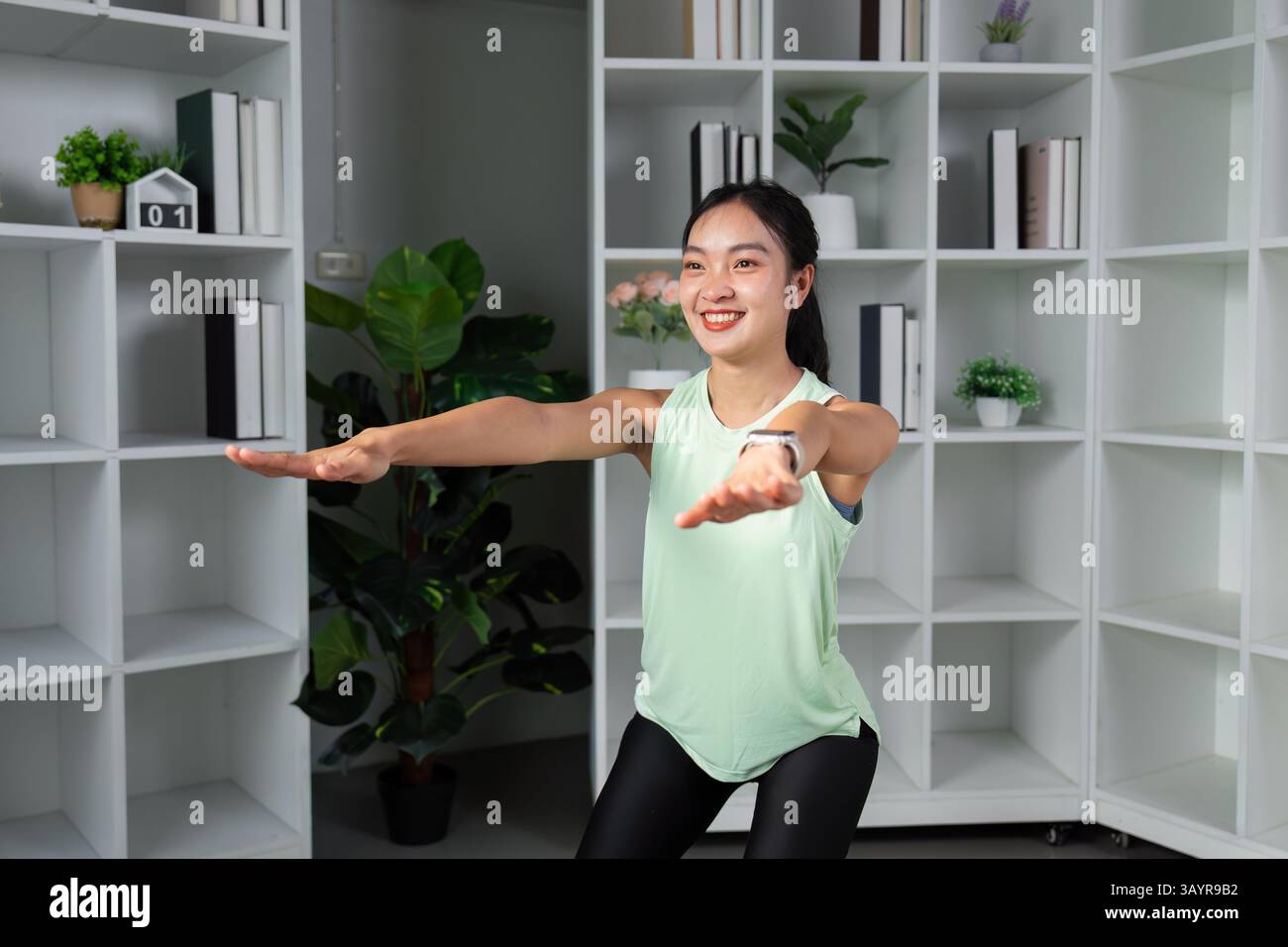 Fitness ed esercizio fisico. Una donna che esegue esercizi di equilibrio con un comportamento gioioso in un ambiente domestico motivazionale. Foto Stock